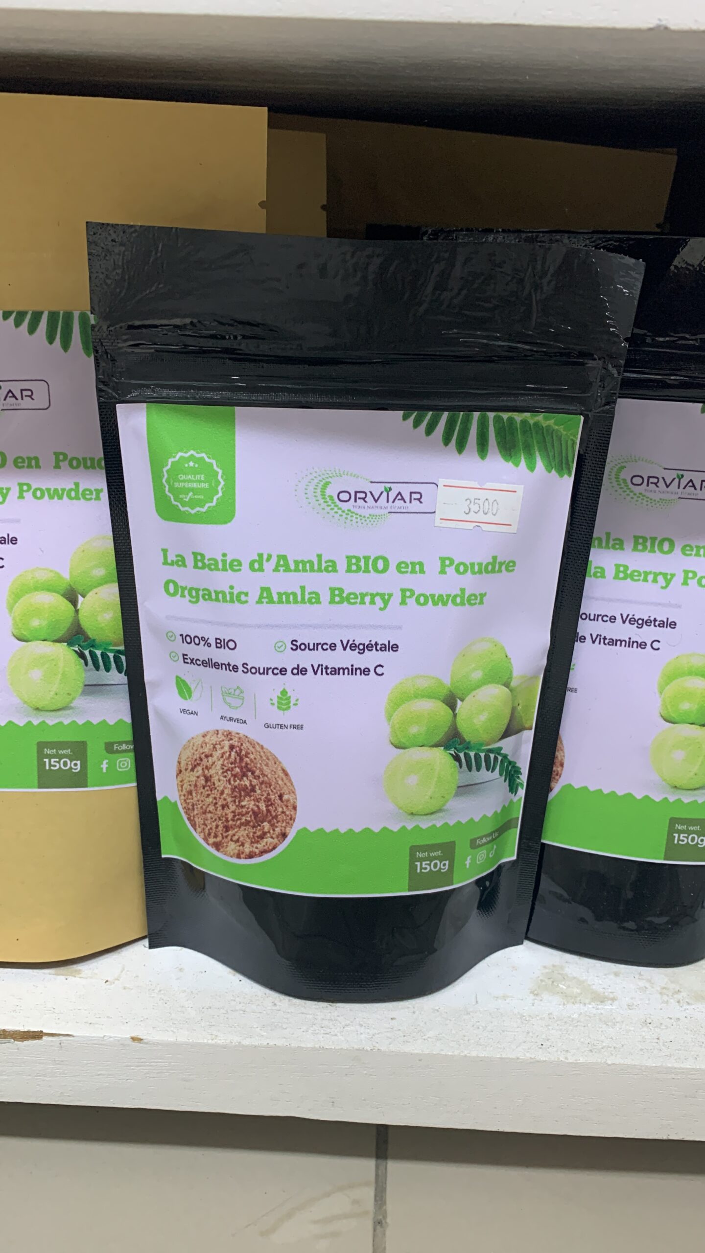 Sachet de Poudre Ayurvédique Triple Action Amla Reetha Bhringraj posé sur un fond naturel avec des feuilles vertes